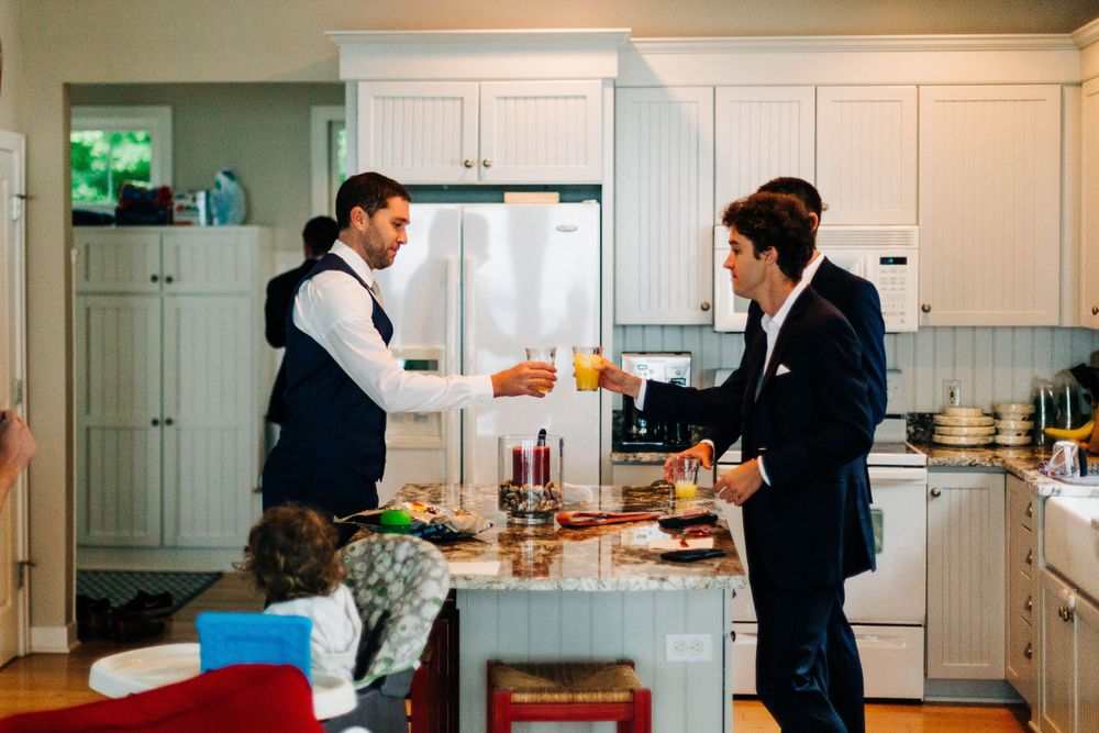 Two people in formal attire having drinks at kitchen counter.