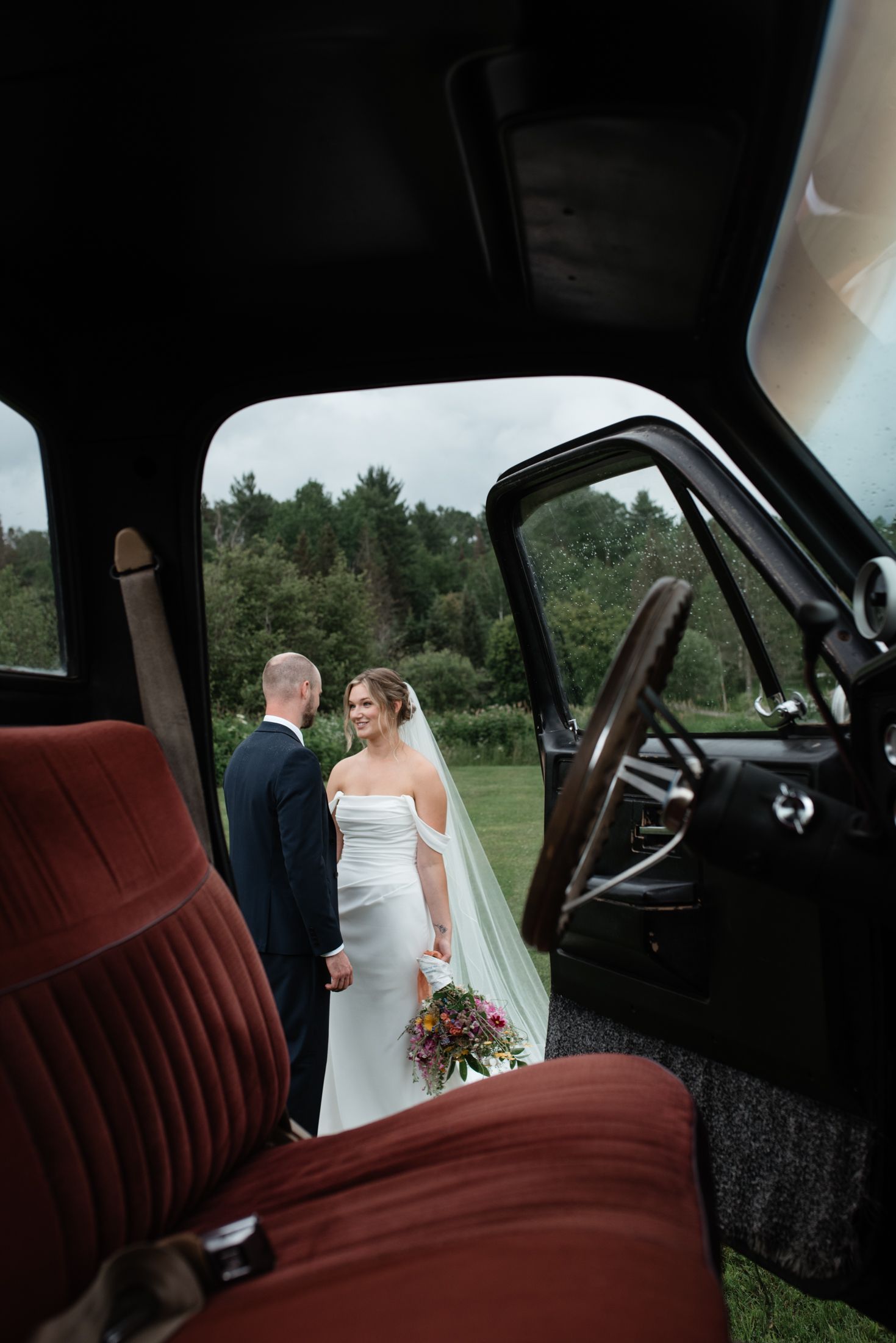 Wedding couple viewed through vintage car window with red interior.