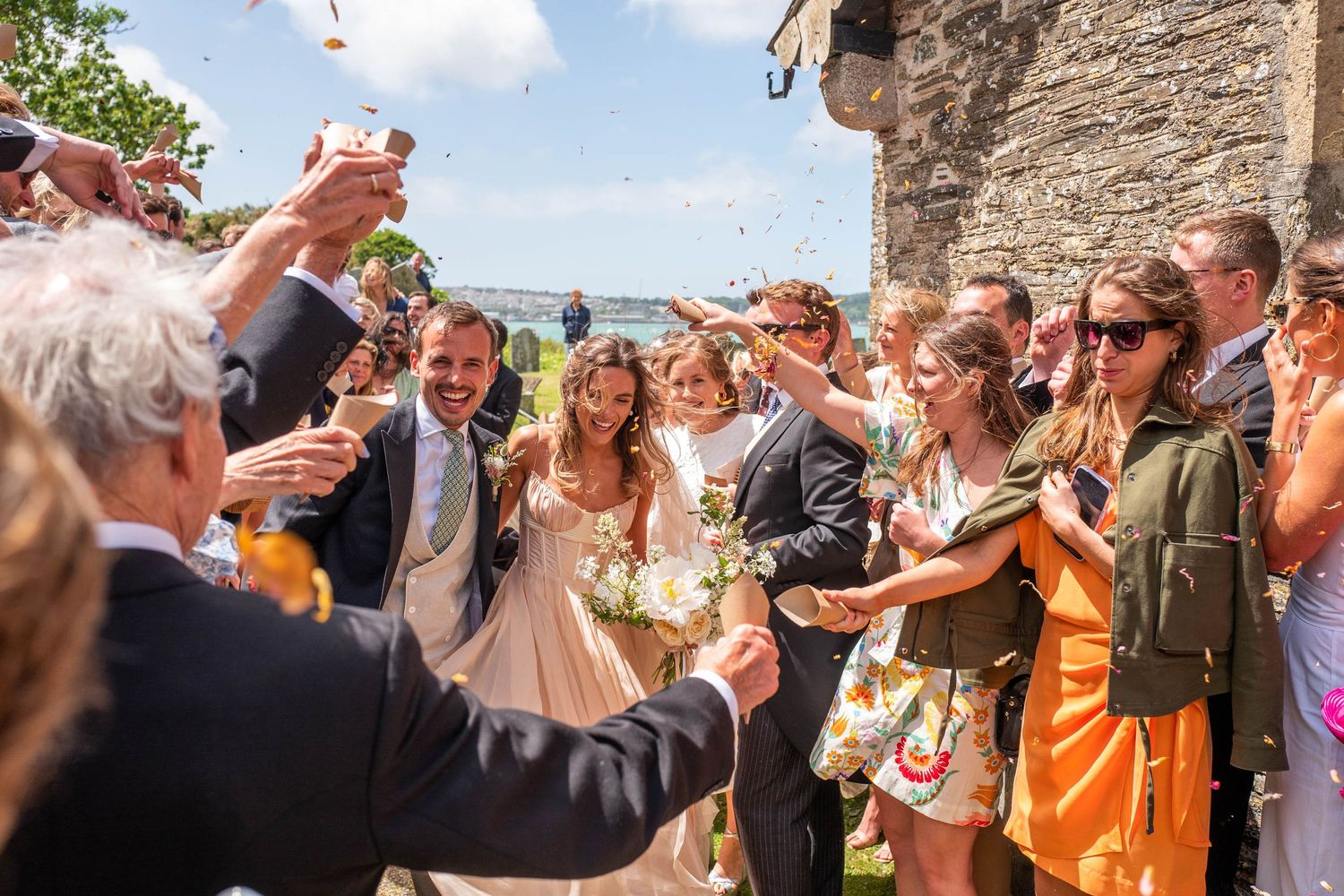 Festive outdoor celebration with guests toasting and cheering on a sunny day.