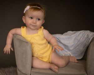 A baby girl is draped over the side of a mini couch