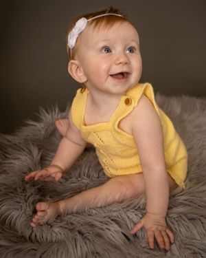 A baby girl sits on a furry rug