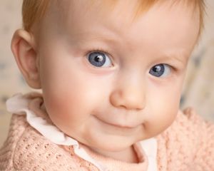 A baby girl with a mischievous smile looks at the camera