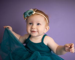 A baby girl plays with her dress with arms to the sides