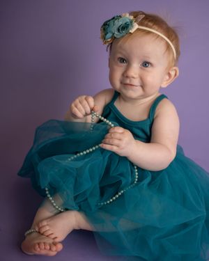 A baby girl with crossed legs plays with some costume jewelry