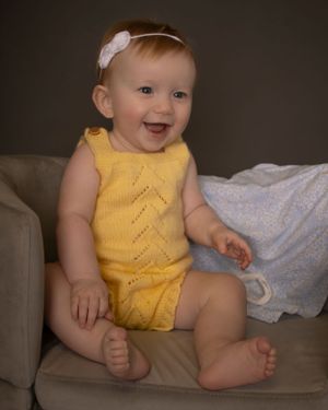 A baby girl laughs while sitting on a miniature couch