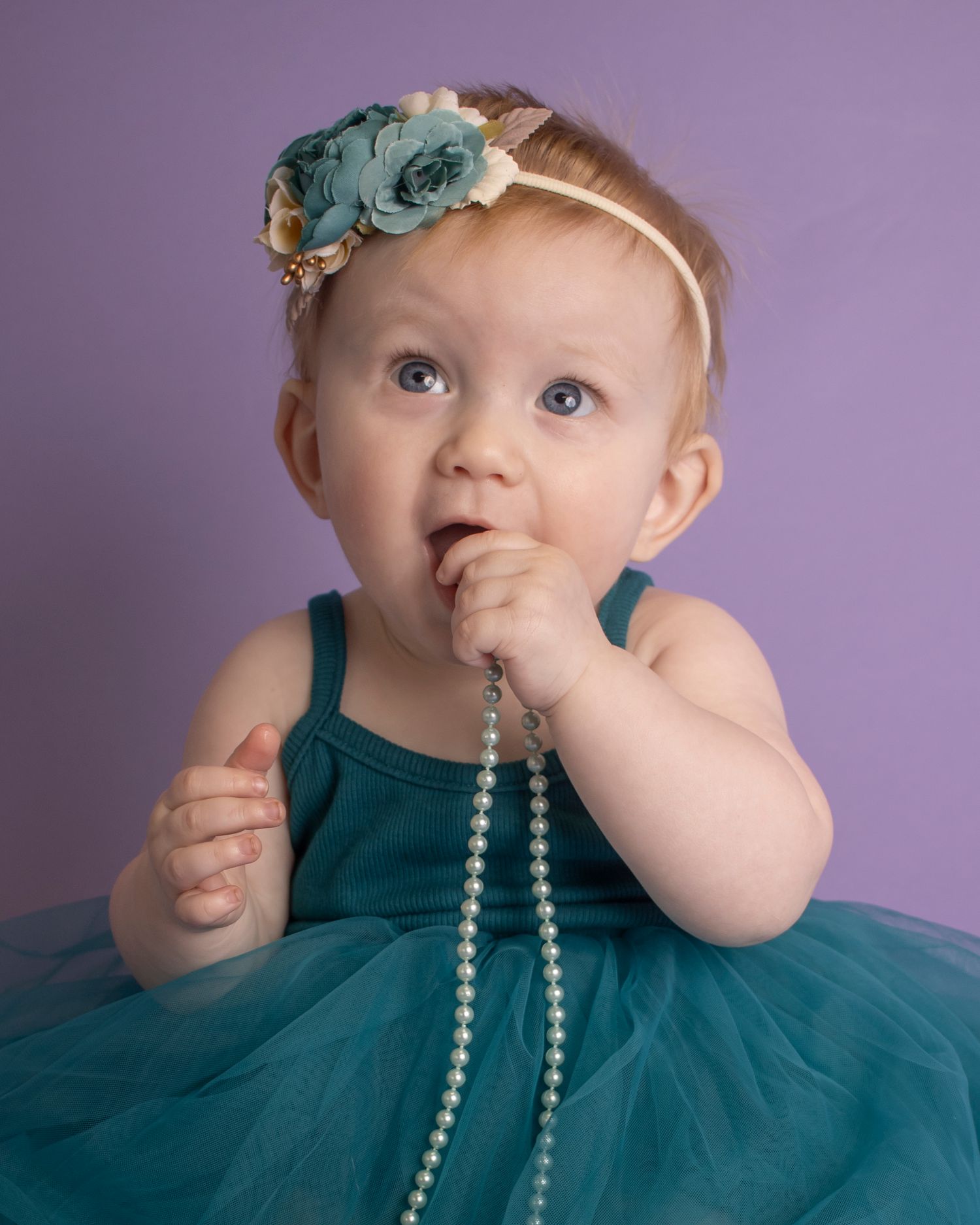 A baby girl mouths a set of costume pearls