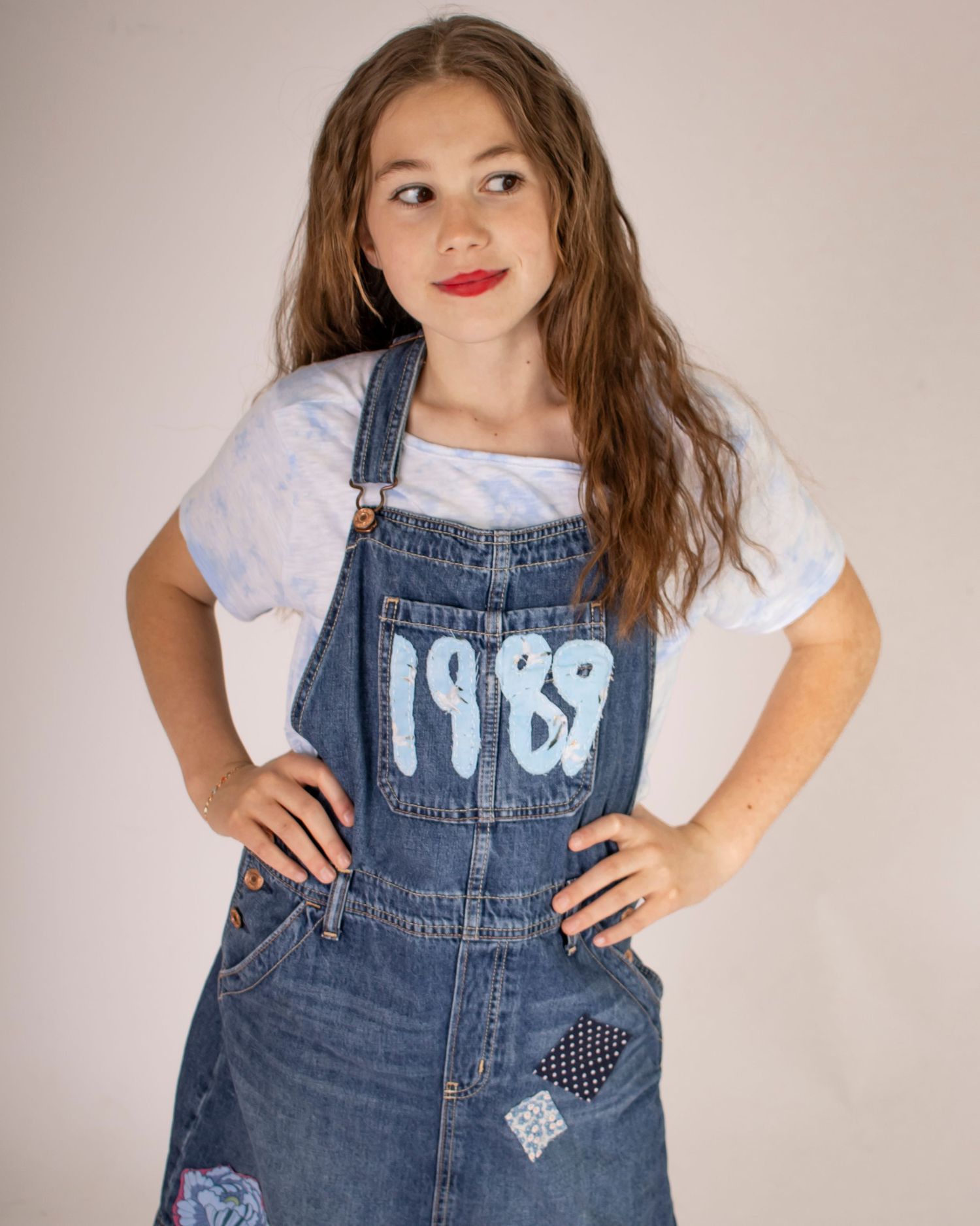 A school age girl stands looking to the side with a tilted smile and hands on her hips