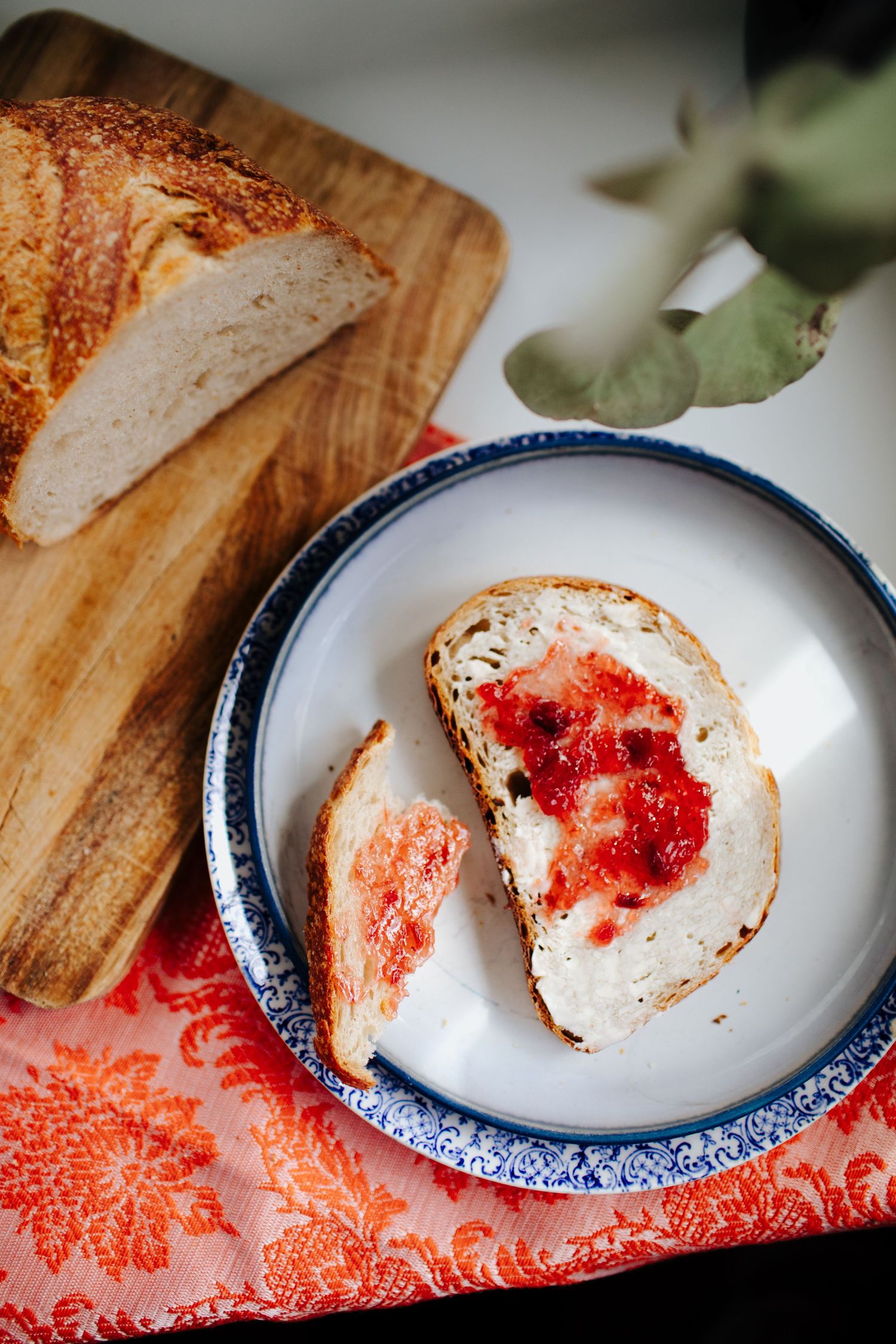 Sliced sourdough bread with red jam spread on a blue and white plate.