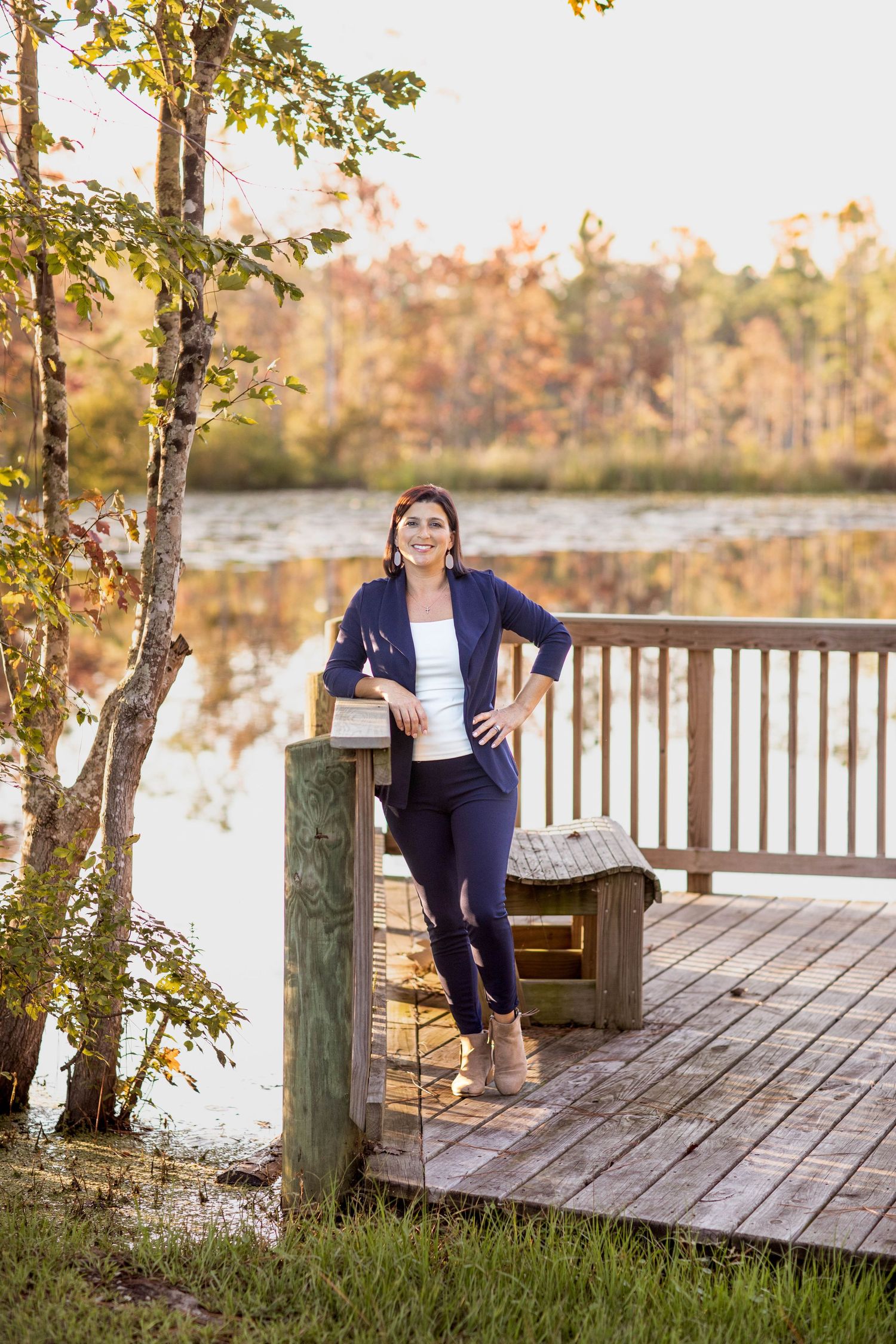 Woman in navy outfit standing on wooden dock by autumn lake.