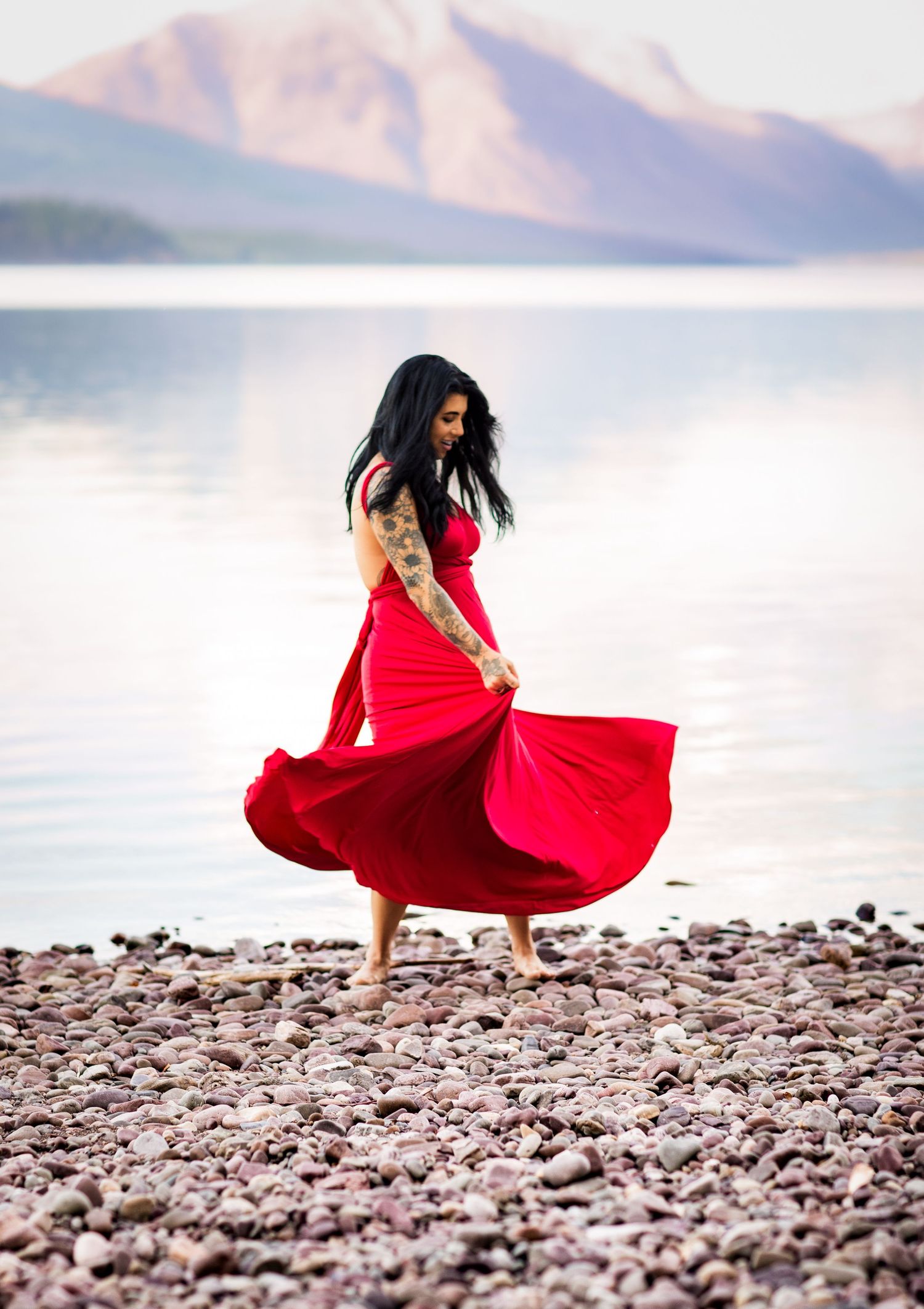 A flowing red dress twirls dramatically against a rocky beach landscape with mountains in the background.