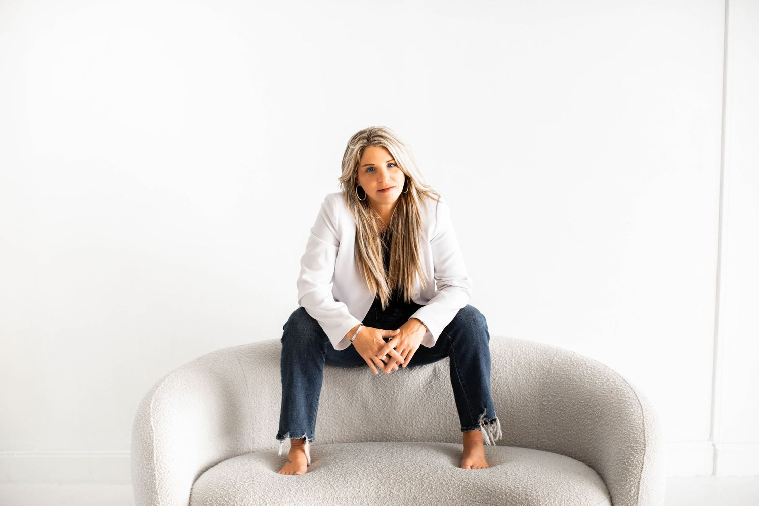 A person on a white couch holds a cup while looking thoughtful and contemplative in a bright minimalist setting.