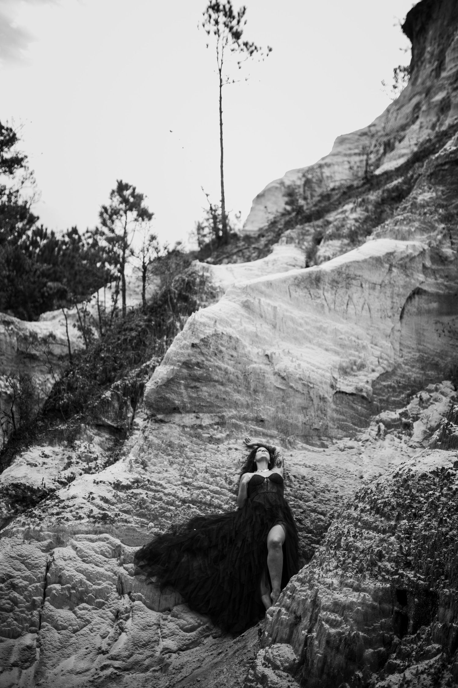 A dramatic black and white photo of a person in dark clothing reclining against a textured rock formation.