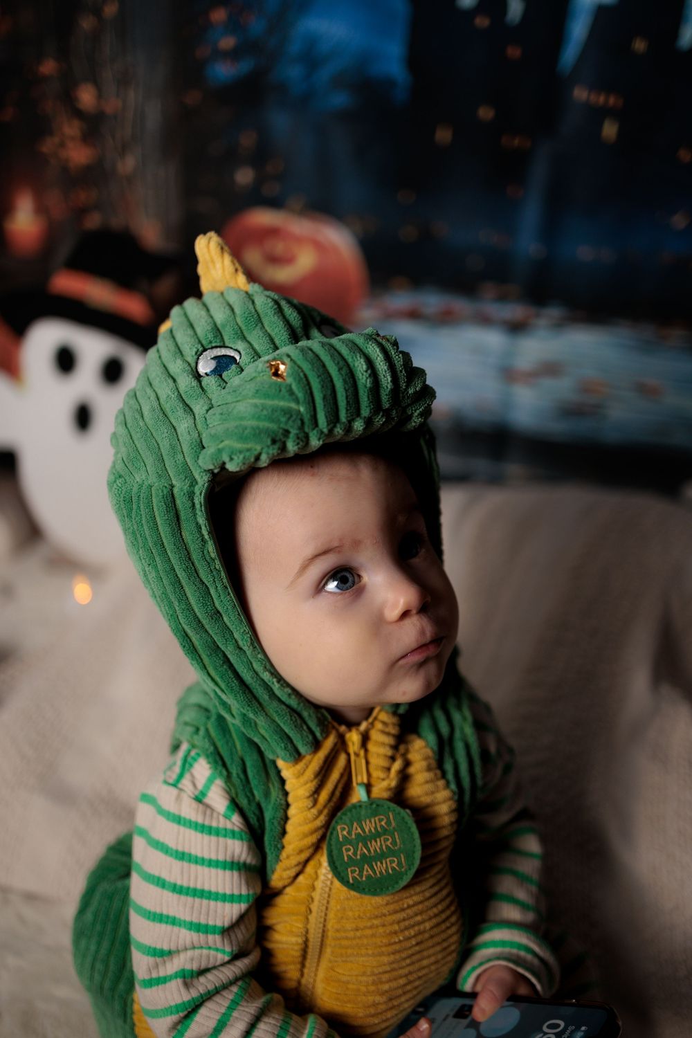 Adorable baby wearing green dinosaur costume with RAWR badge in festive holiday setting.