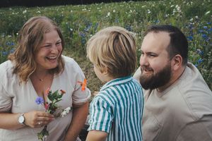 Happy family with young boy holding wildflowers laughing together in a flower field.