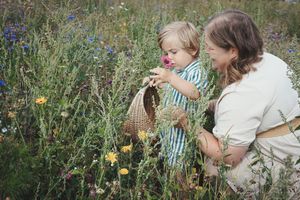 Mother and toddler picking wildflowers together in a colorful meadow, child holding a wicker basket.