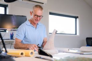 Professional in light blue polo works at desk reviewing architectural documents.