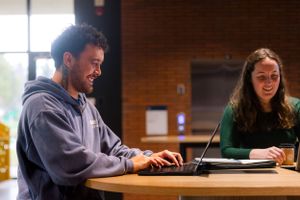 Two students study together at a wooden table in a university setting.