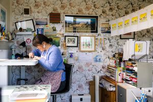 A panoramic view of an art studio workspace with floral wallpaper, drawings, and creative materials displayed throughout.