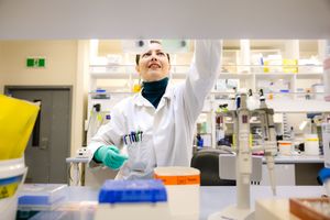 Scientist in white lab coat and gloves working in a modern research laboratory with equipment and supplies.
