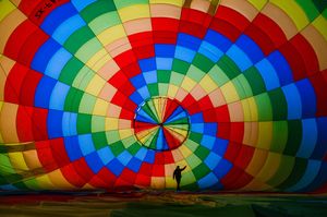 Person standing inside a vibrant colorful hot air balloon with rainbow pattern of red, blue, green, and yellow panels.