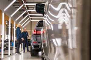 Two people inspect a modern SUV in a bright automotive showroom with overhead lighting.