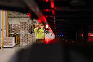 Warehouse worker in yellow vest tying down curtain sider of large long haul truck