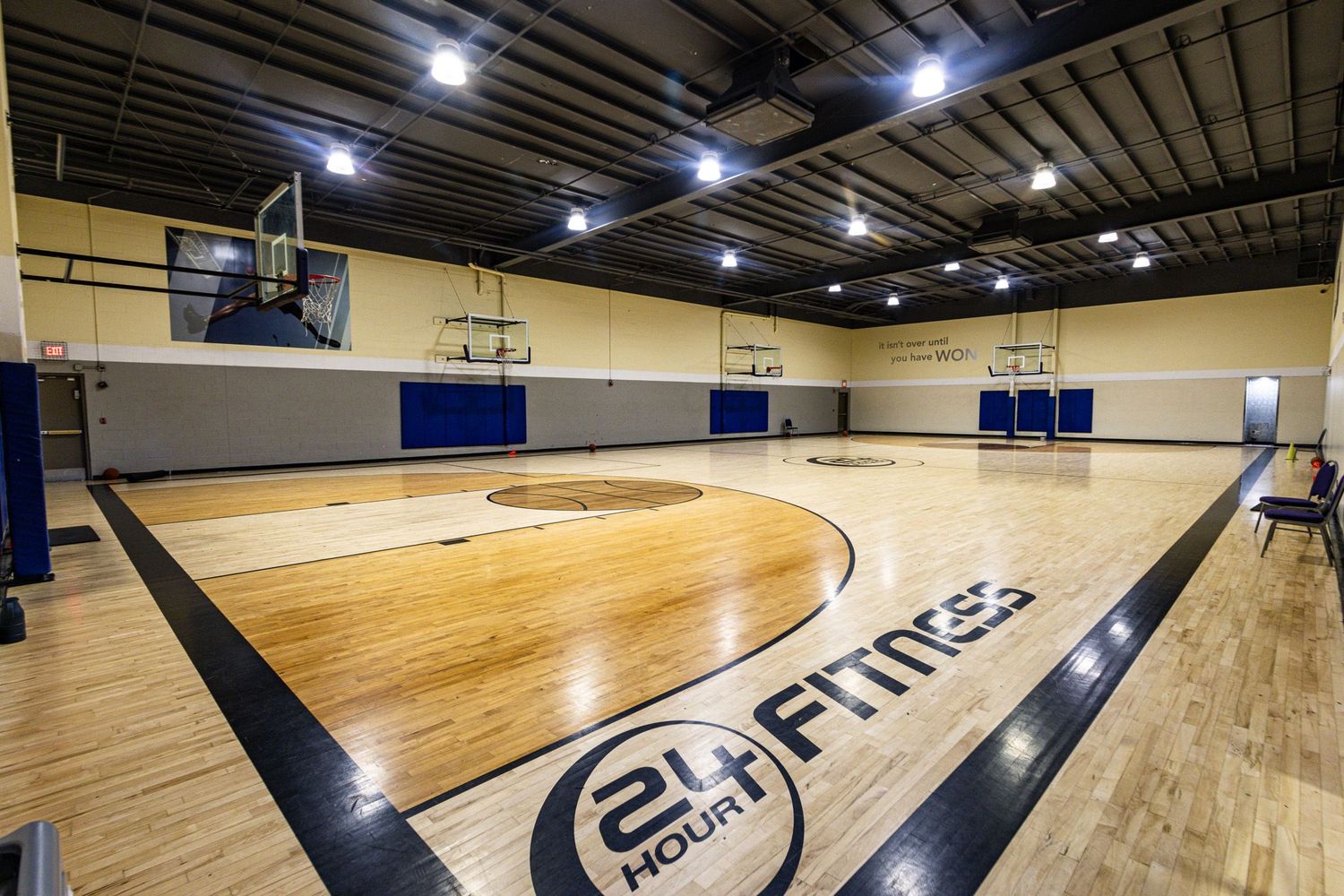 An indoor basketball court inside a 24 Hour Fitness gym, featuring polished hardwood floors and the company logo on the court.
