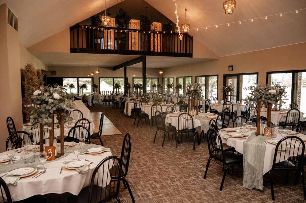 Elegant wedding reception hall with round tables, white linens, black chairs, and string lights.