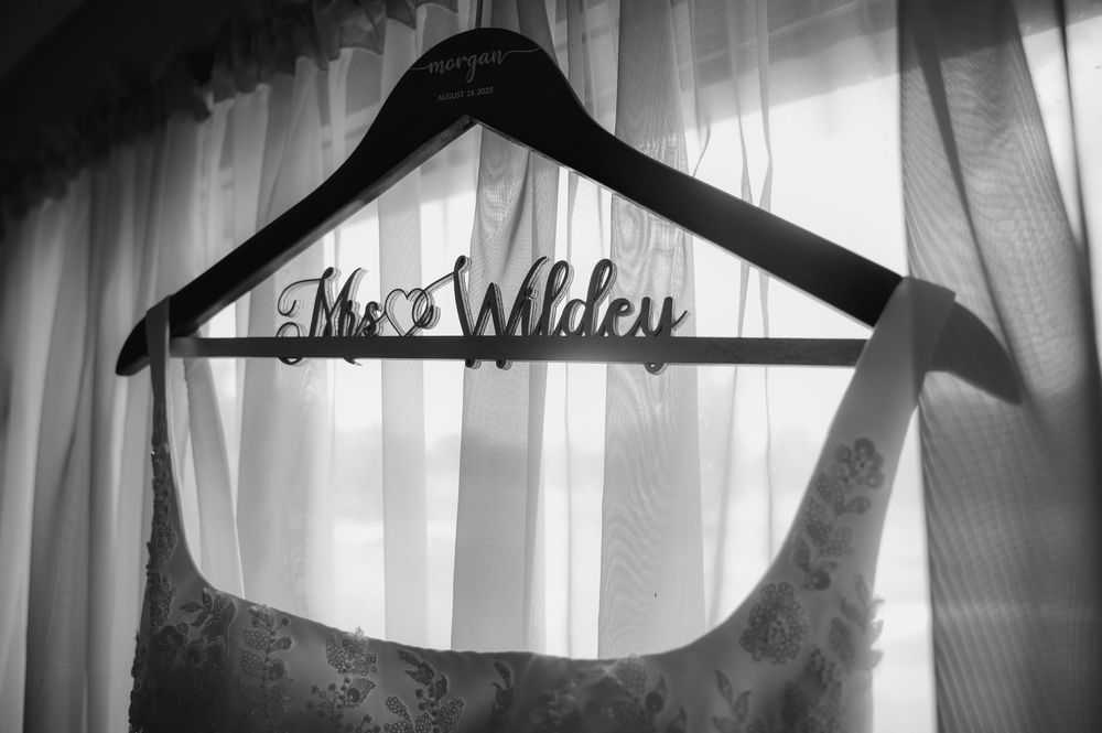 Black and white photo of The Willey wedding dress hanger with gown against sheer curtains.