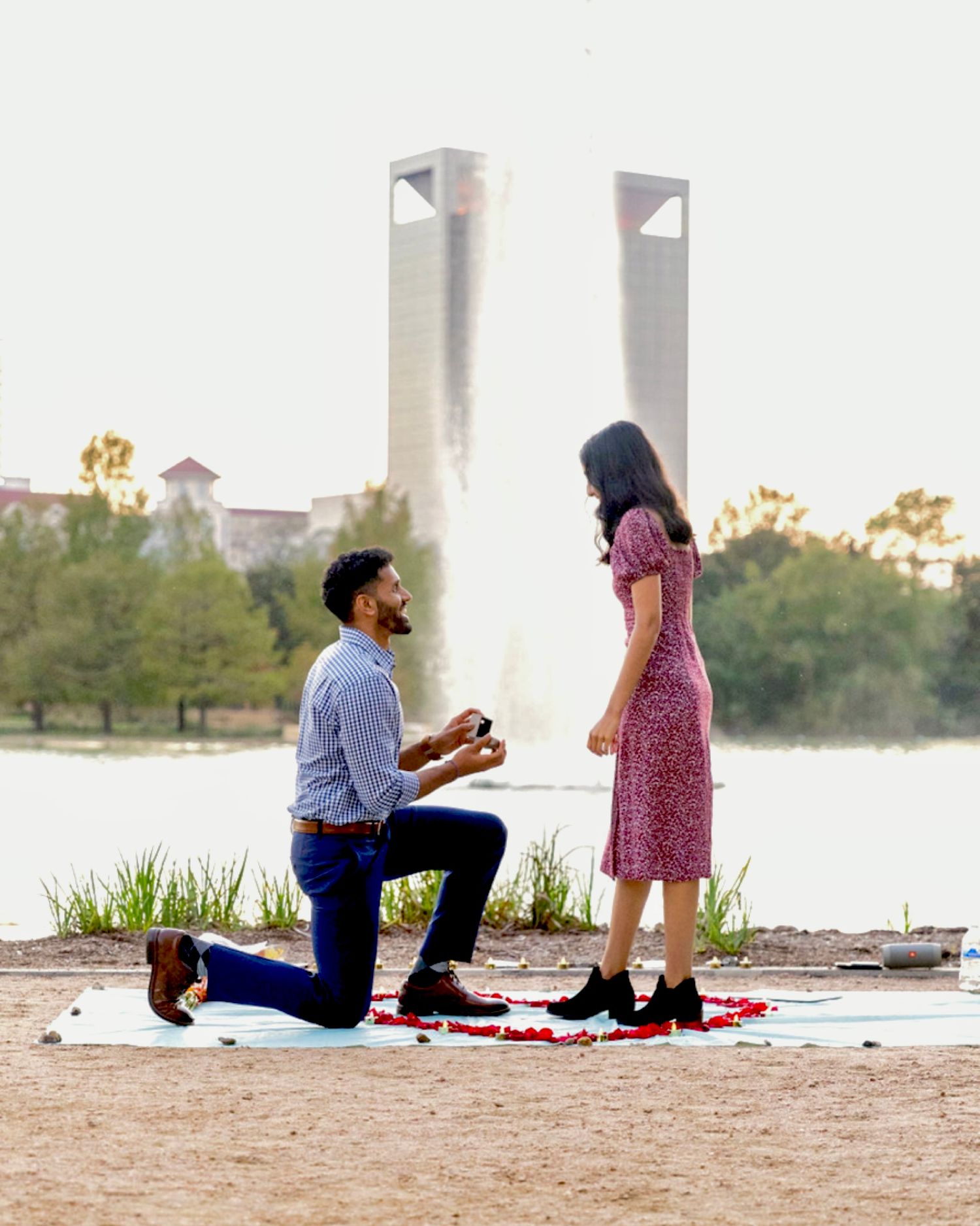 Man proposing on one knee to his partner outdoors near a scenic fountain.