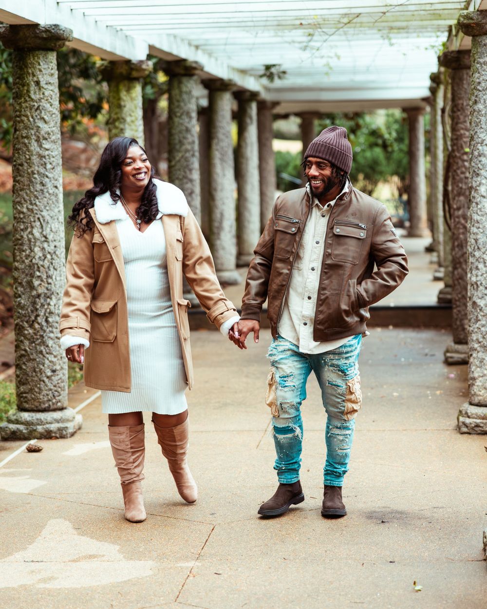Happy couple walking hand in hand through columned garden path, laughing and smiling together.