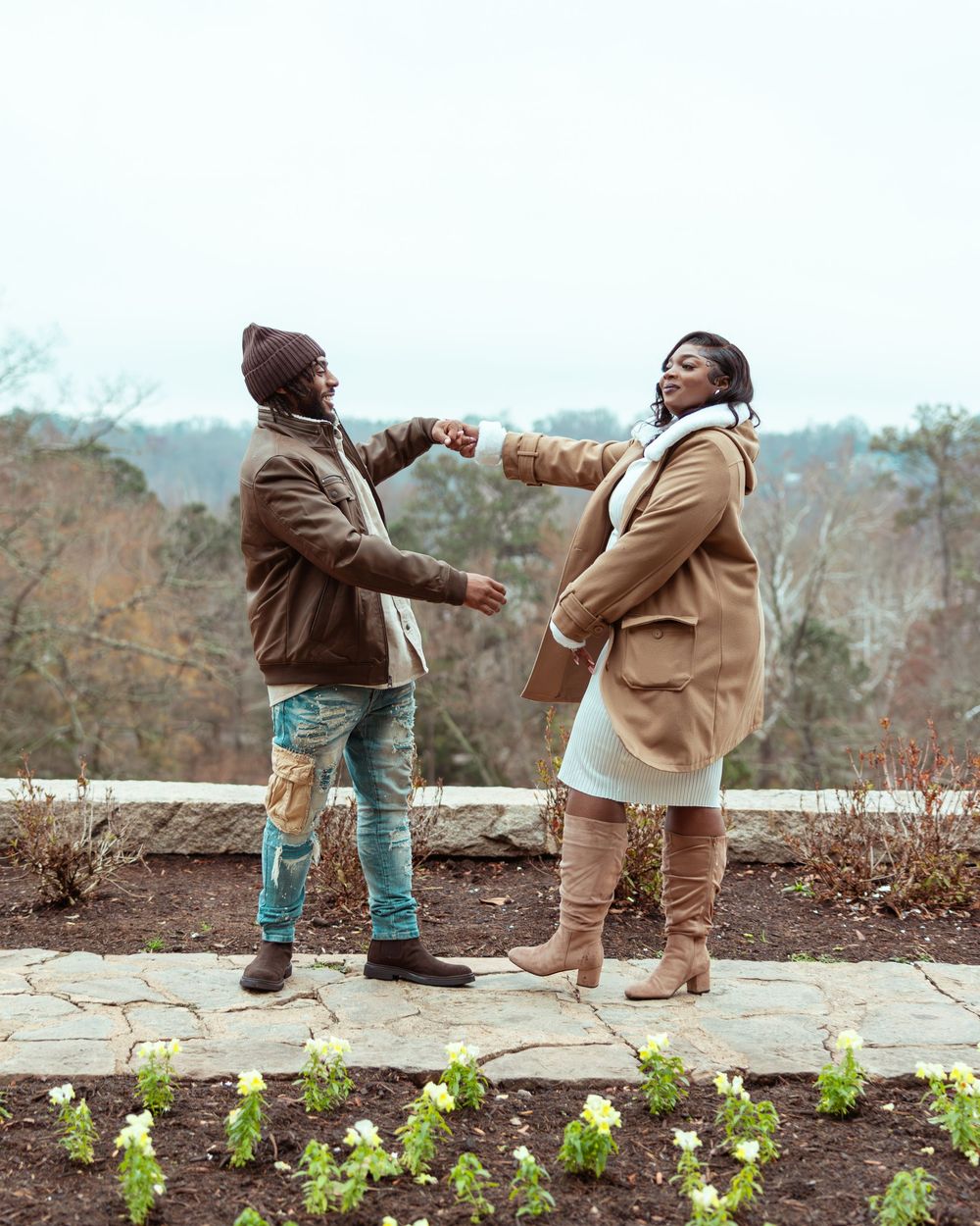 Playful couple dancing together on stone terrace overlooking autumn landscape in stylish fall outfits.