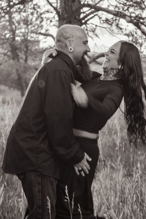 Black and white photo of tattooed couple laughing together in tall grass field.
