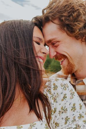 Romantic couple smiling and touching foreheads together outdoors near a peaceful waterway.