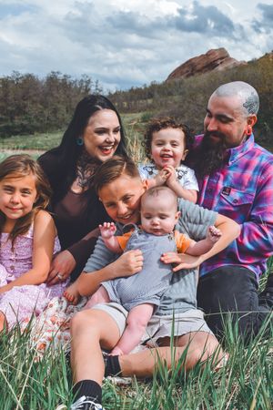 Joyful family of six sharing a candid moment outdoors in a grassy field with red rocks.
