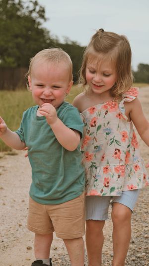 Two happy toddlers playing outdoors on a dirt path, boy in teal shirt and girl in floral dress.