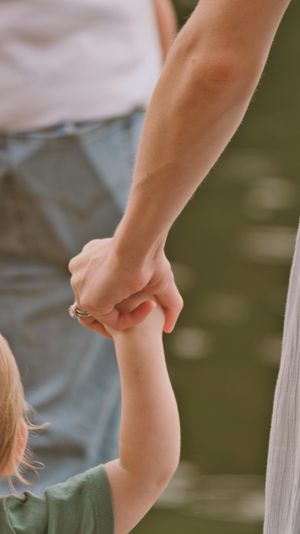 An adult holding a young child's hand outdoors near water, wearing a silver ring, symbolizing family love and connection.