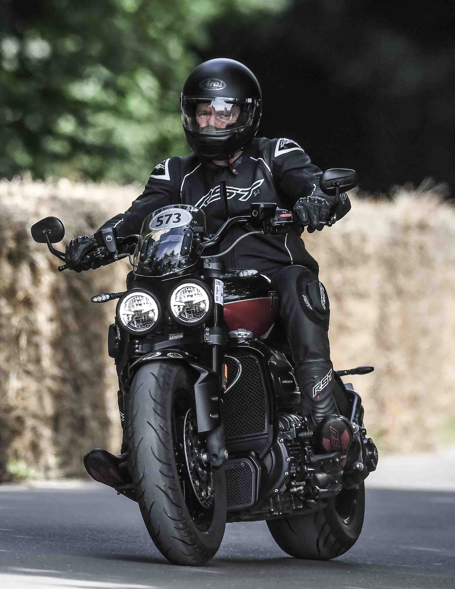 Motorcyclist in full black gear rides a modern sport bike on a curved road.