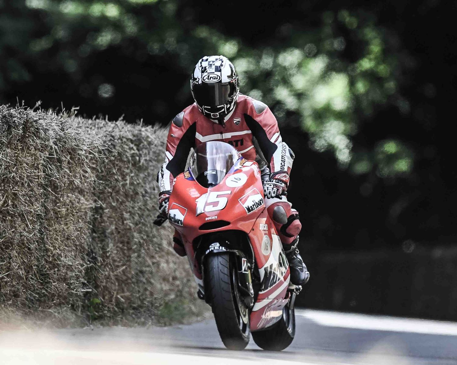 A motorcyclist in red racing gear rides a red sport bike on a curvy road.
