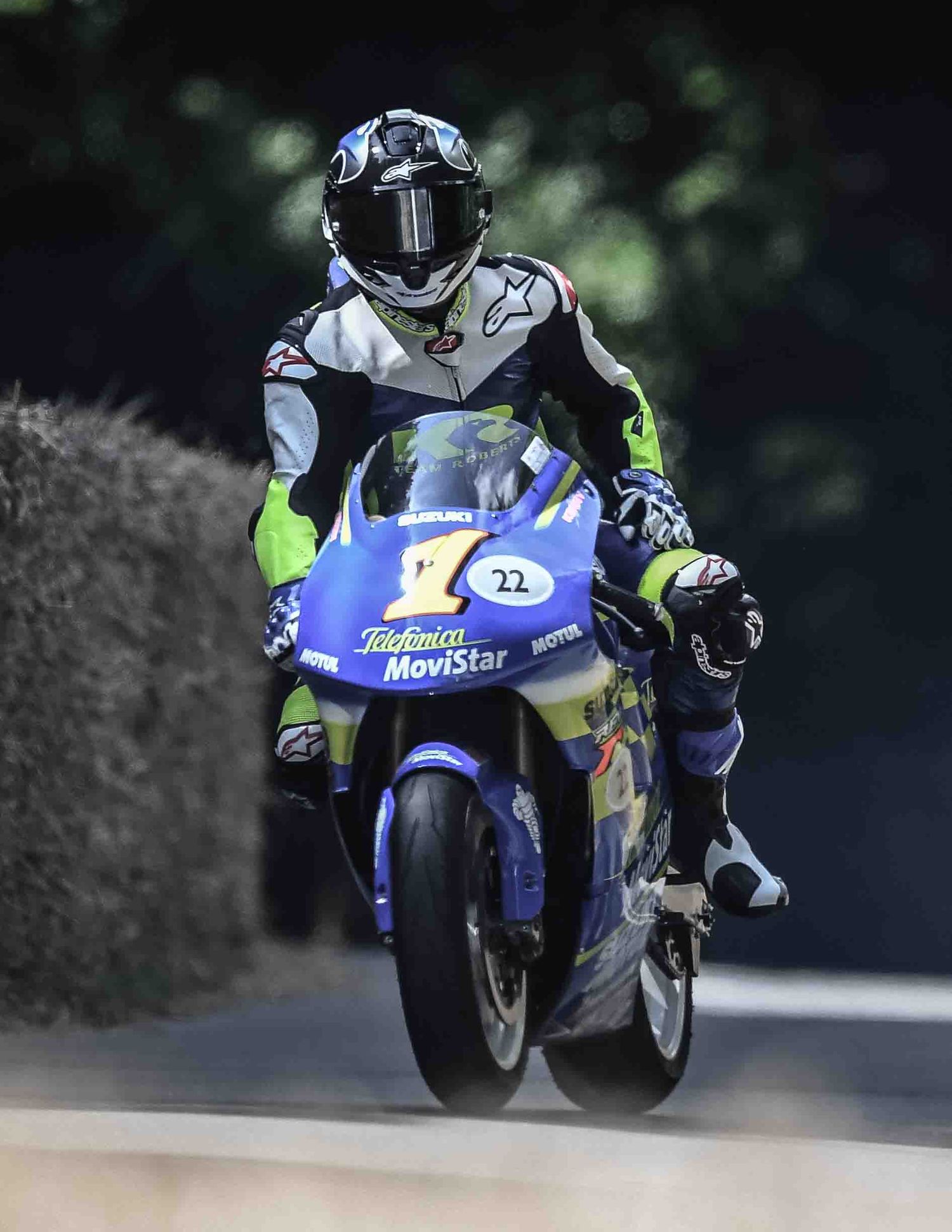 A motorcycle racer leans into a turn on a blue sport bike during competition.