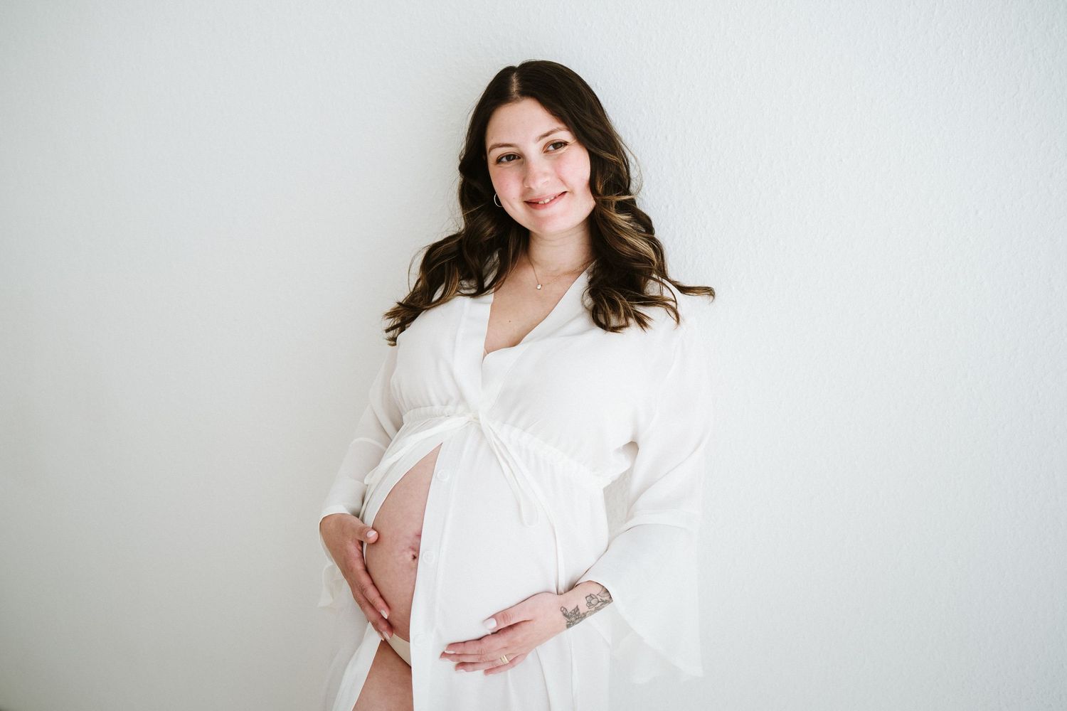 Maternity photo session in white studio with soft lighting.
