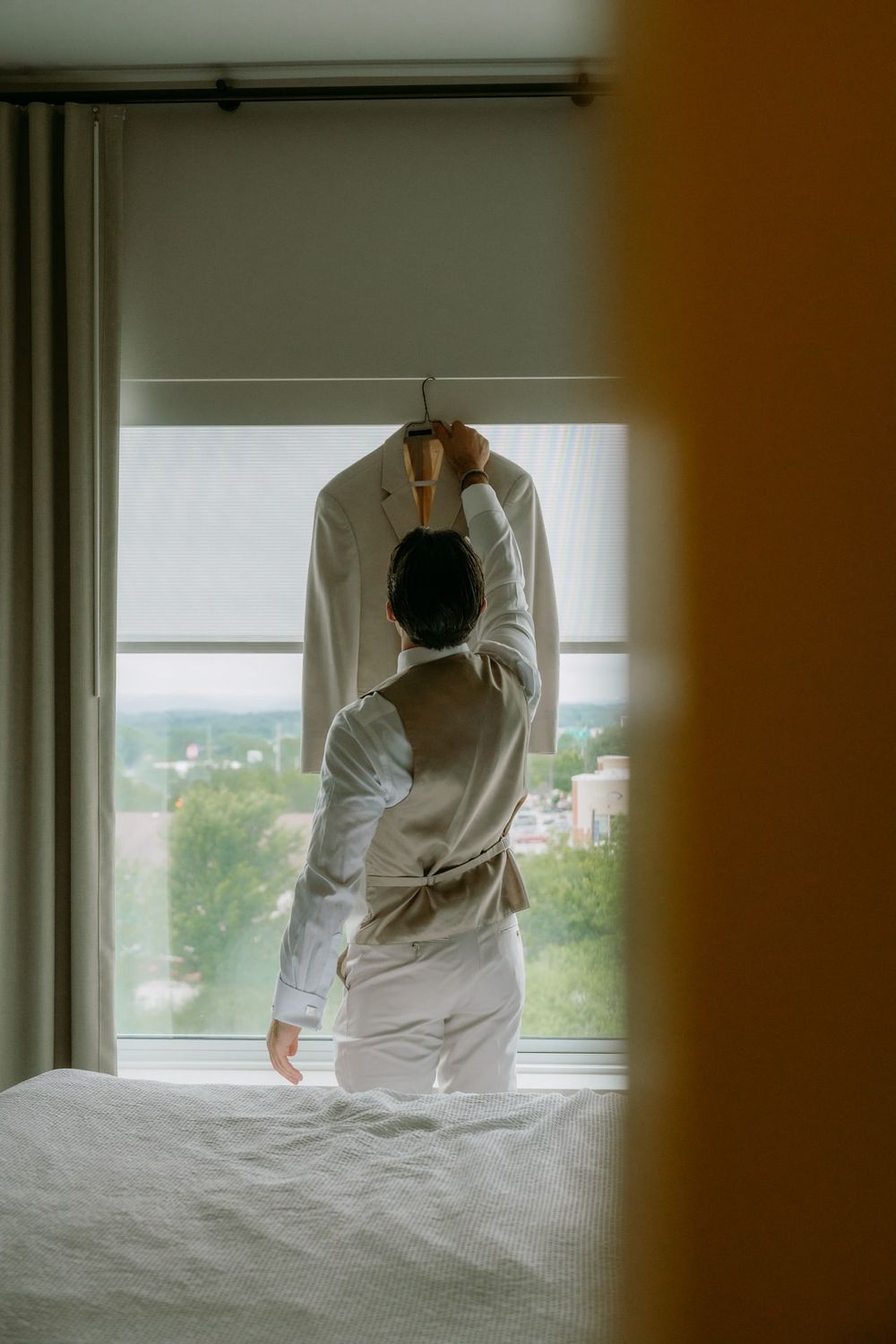 Someone hanging a white dress shirt on a window rod in a bright room.
