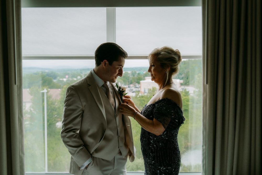 An intimate moment captured as someone helps adjust a tie in front of a window with a city view.