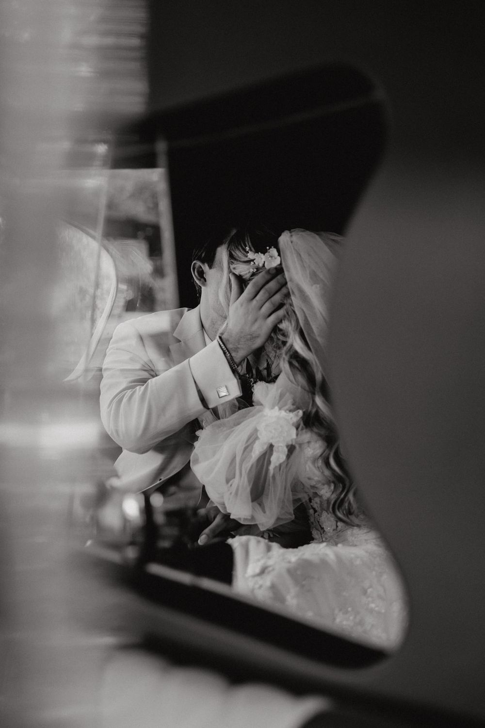 An artistic black and white wedding photograph showing intimate moments through reflective surfaces.