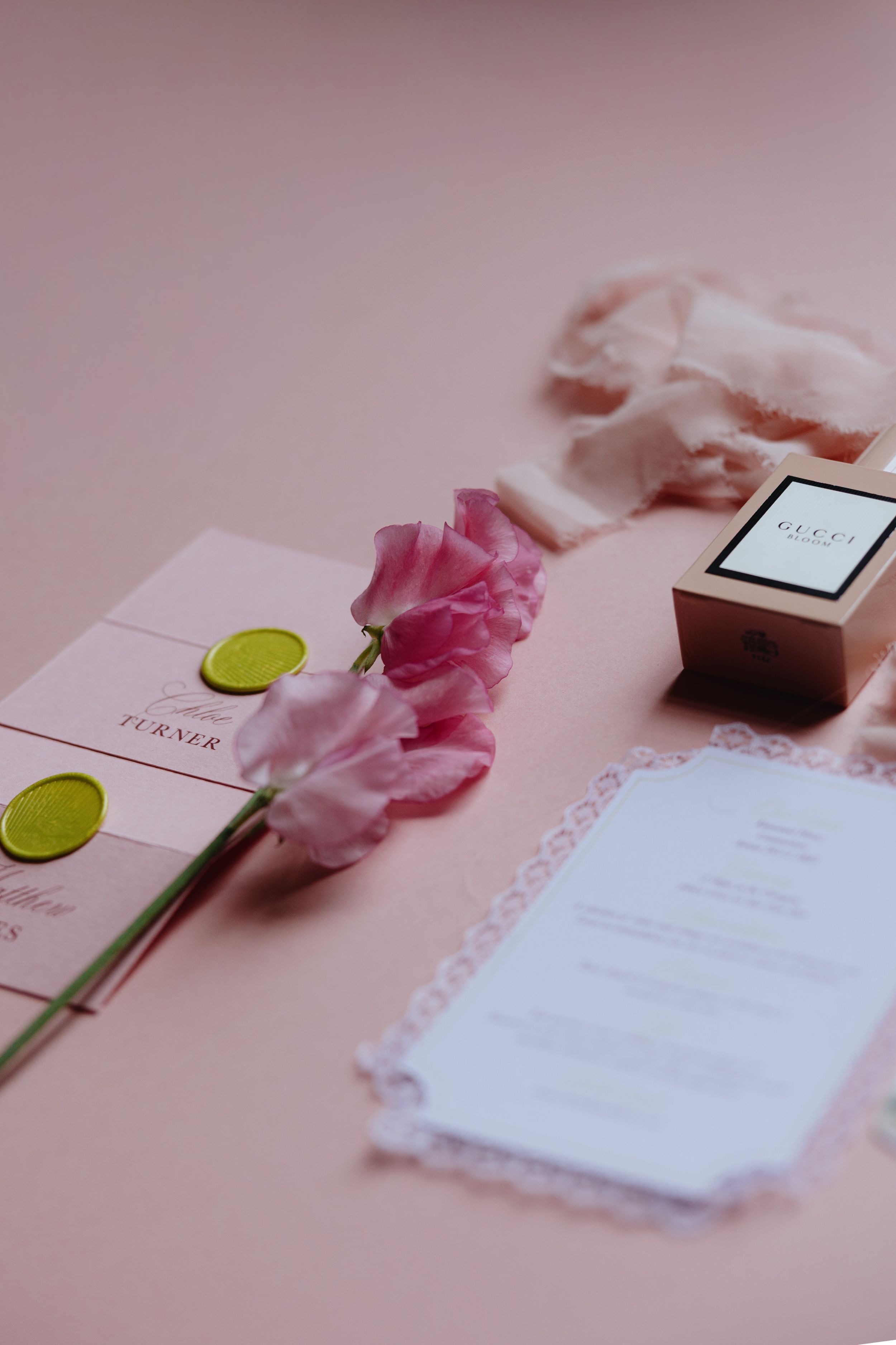 Pink wedding stationery with wax seals, a pink tulip, Gucci box, and ribbon on a blush background.