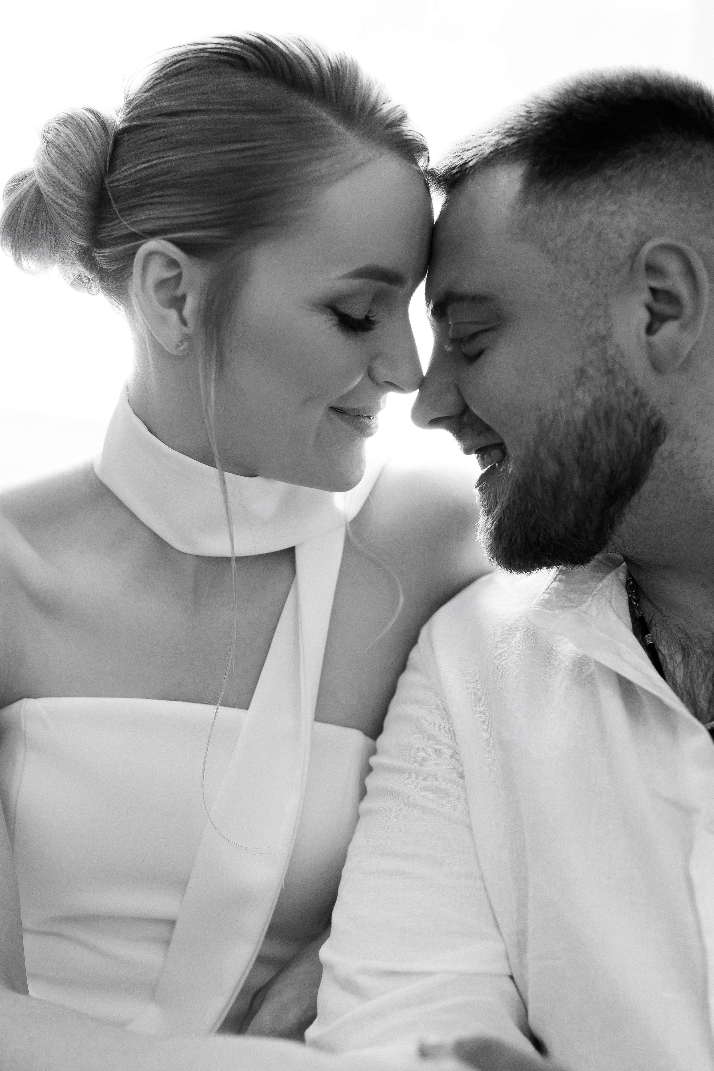 Black and white photo of a smiling bride and groom leaning foreheads together in a tender romantic moment.