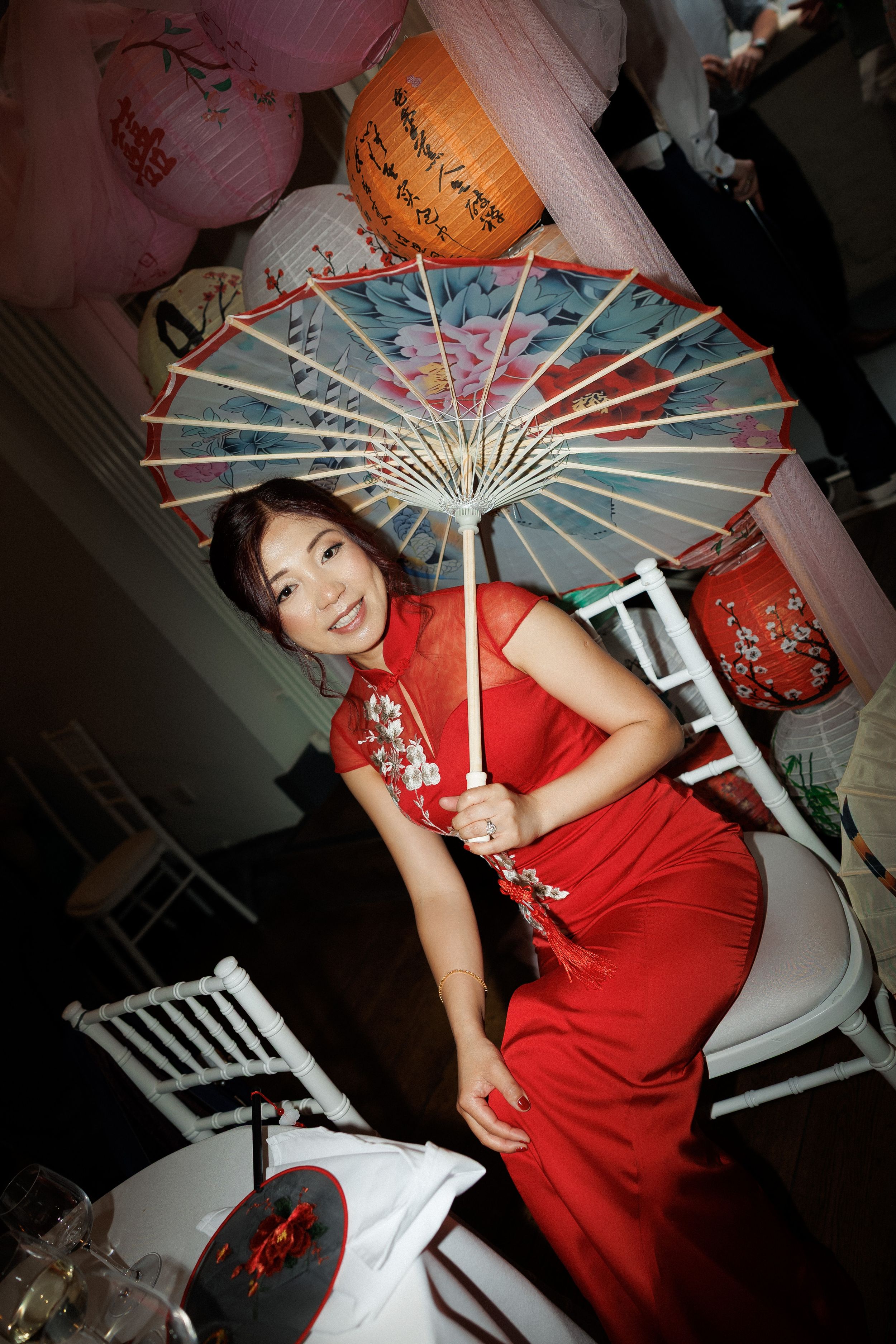 Woman in red qipao holding a decorative Chinese parasol, surrounded by paper lanterns at an elegant event.
