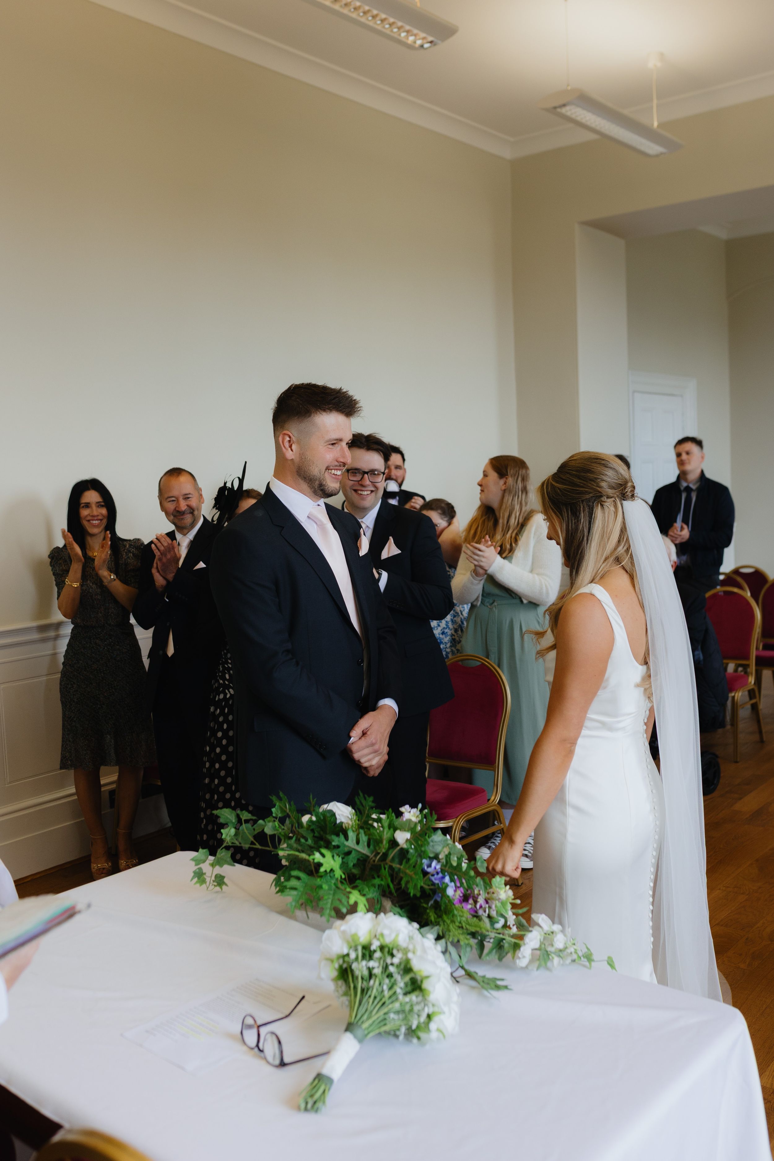 Wedding guests mingle and socialize in an elegant indoor venue with white walls and hardwood floors.