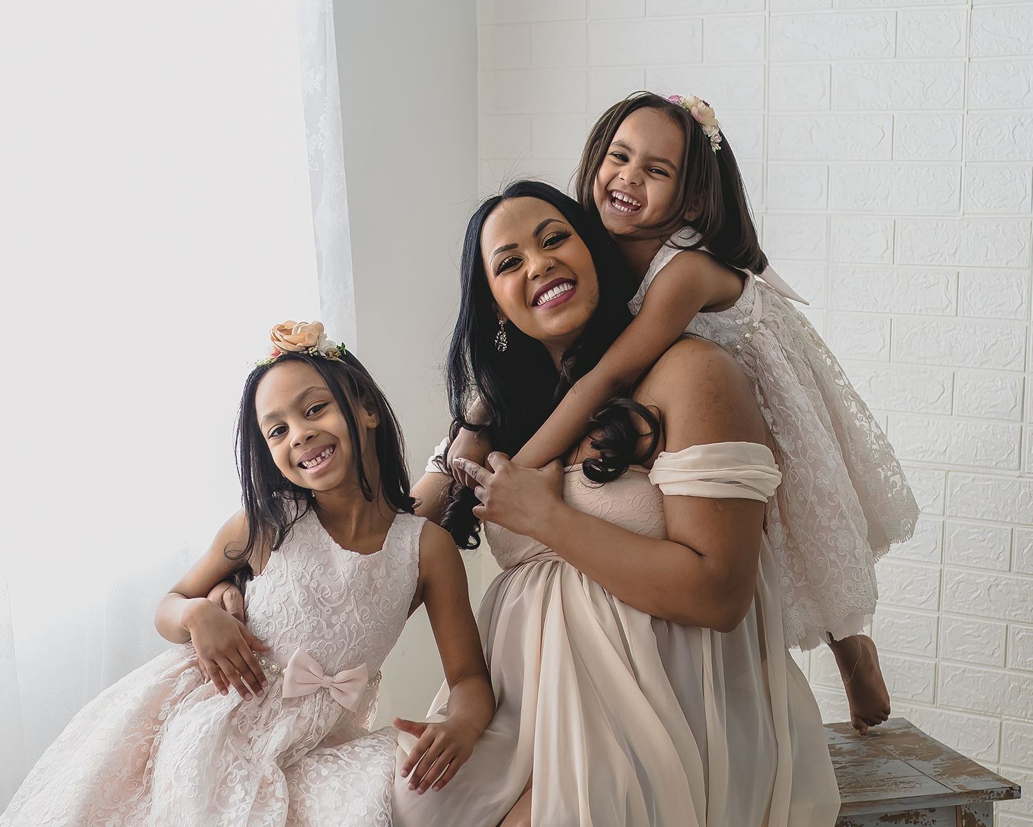 Candid family photo showing laughter and embraces in cream and white dresses against white backdrop.