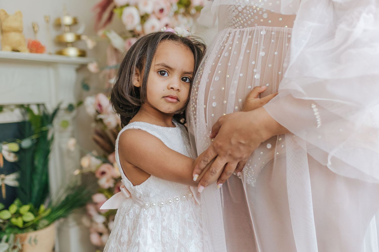 A child in a white lace dress touches delicate white fabric in an elegant indoor setting.